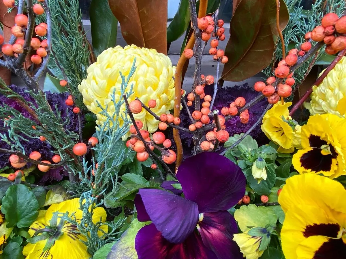 Orange winterberry, magnolia leaves and yellow pansies in a winter arrangement